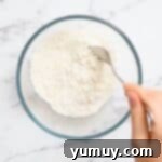 A fork stirring all-purpose flour in a microwave-safe bowl, ensuring even heat distribution during the cooking process.