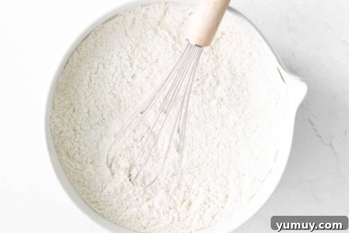 A close-up shot of a mixing bowl filled with all-purpose flour, alongside a whisk, ready for the heat treatment process.