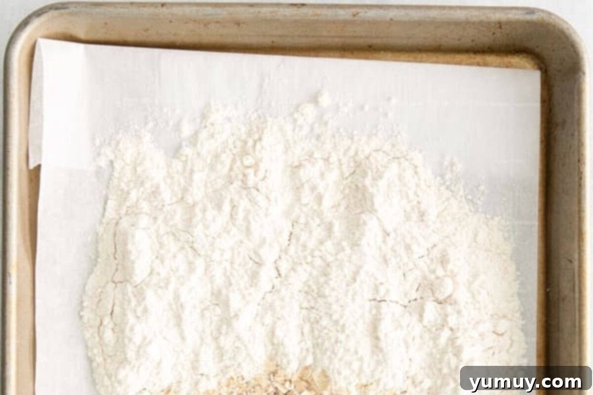 All-purpose flour thinly spread out on a baking tray lined with parchment paper, ready for oven heat treatment.