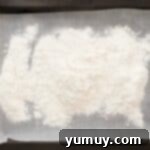 All-purpose flour spread out evenly on a parchment-lined baking tray, ready for heat treatment in the oven.