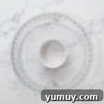 Instant Monkey Bread Delight 4 A greased glass pie dish with a ramekin positioned in its center, ready for the biscuit pieces.