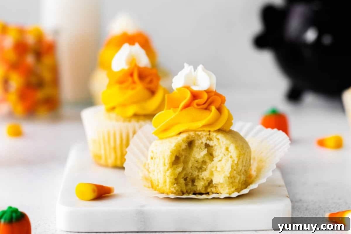 an unwrapped and bitten candy corn cupcake on a marble serving tray.