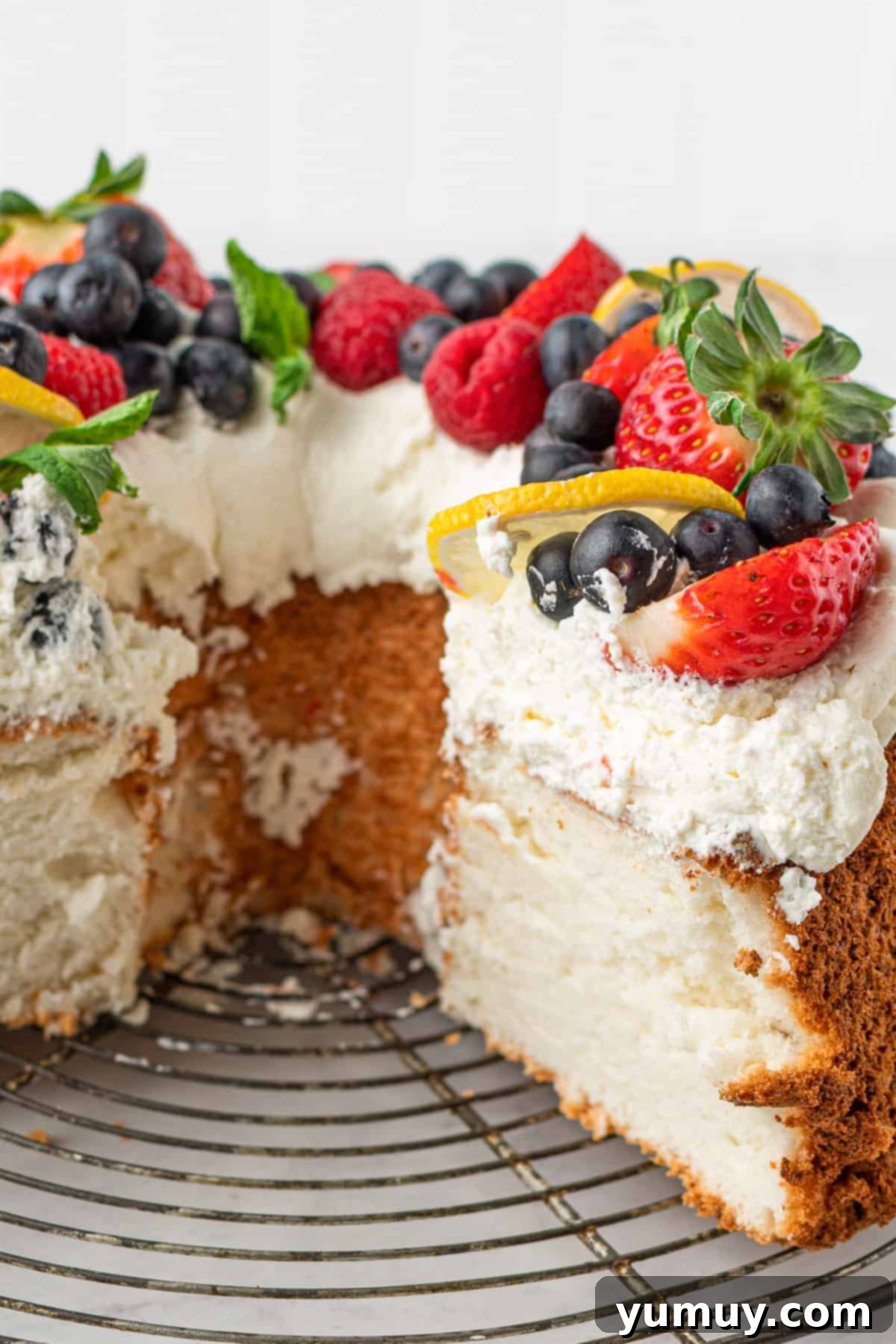 Sliced lemon angel food cake garnished with whipped cream and fresh berries, showcasing its light and airy texture.