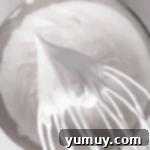 A wire whisk showing a perfect stiff peak of meringue, indicating it is ready.