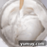 Folding the flour and powdered sugar mixture into the meringue with a rubber spatula in a stainless steel mixing bowl.