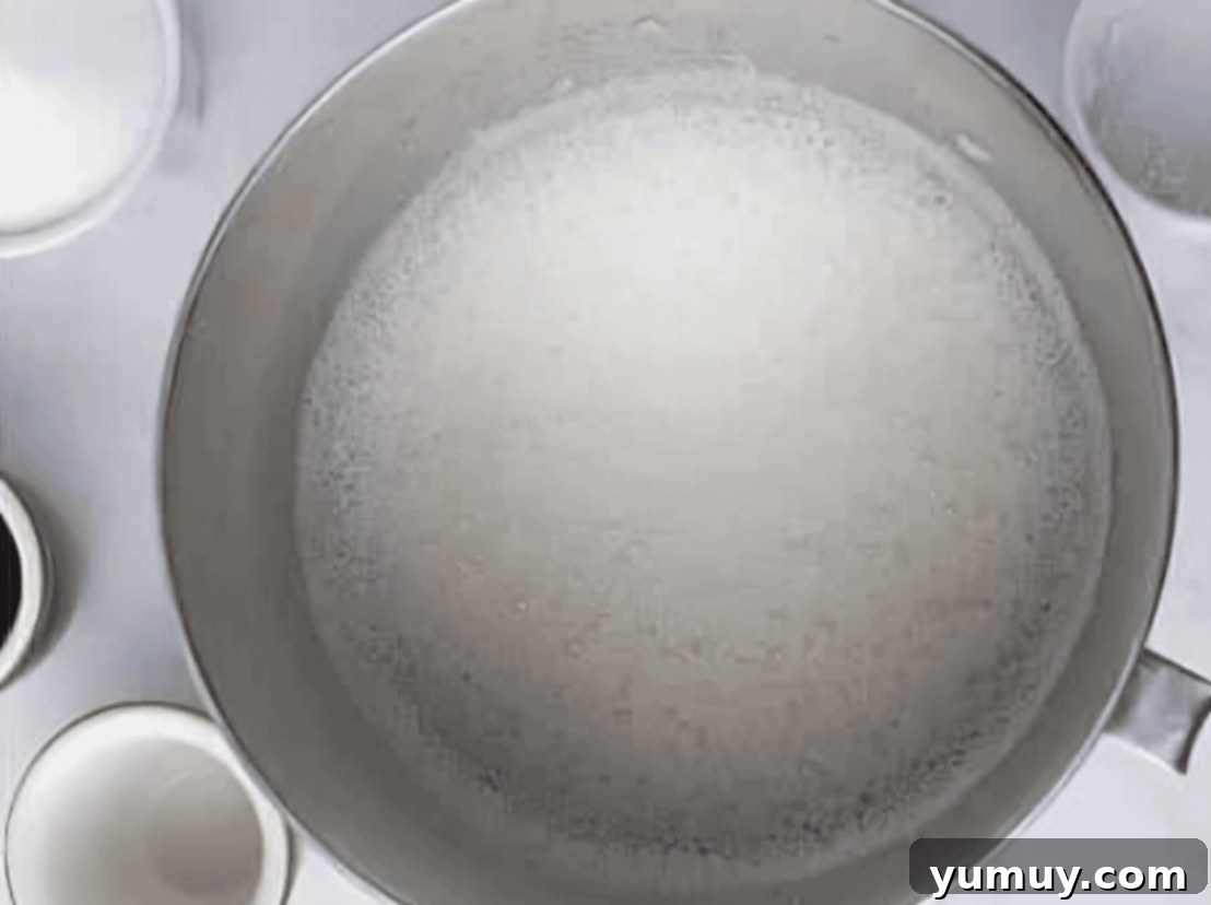 Granulated sugar being slowly poured into the bubbling egg whites in a stand mixer bowl.