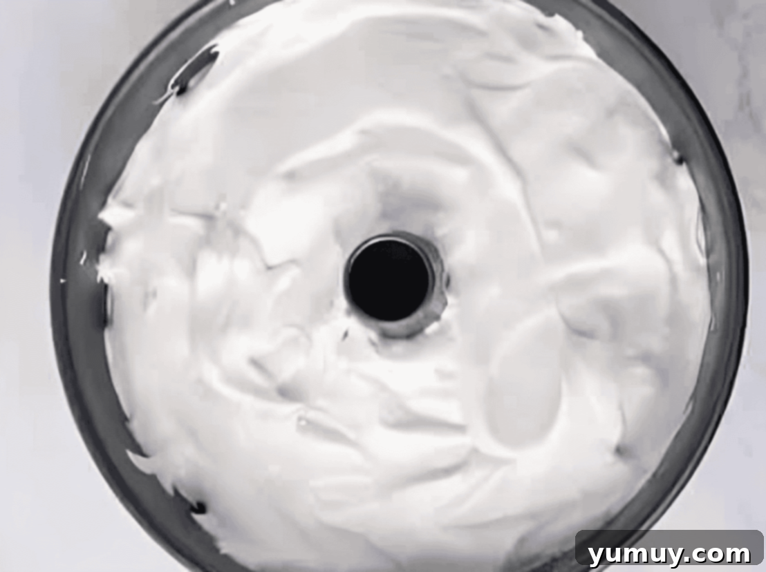 Lemon angel food cake batter being carefully poured and spread into an ungreased tube cake pan.