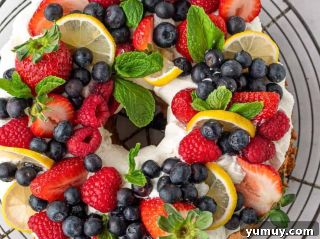 A beautiful lemon angel food cake, adorned with whipped cream and fresh berries, on a wire rack ready to be served.