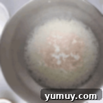 Cream of tartar and kosher salt added to foamy egg whites in a stainless bowl.