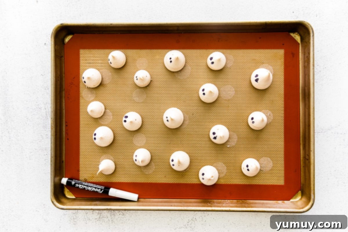 Ghost meringues lined up on a baking sheet, dotted with eyes.