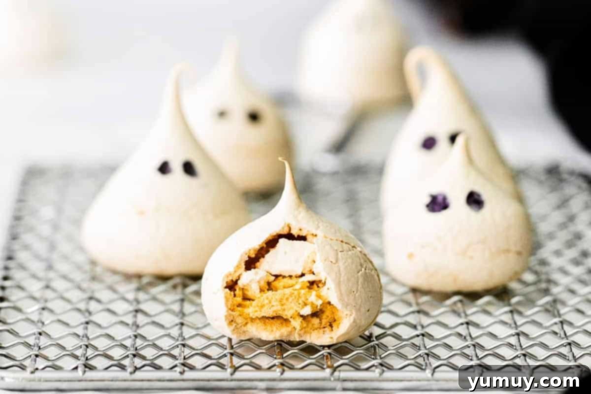 a cracked meringue cookie showing the inside texture on a wire rack next to in tact ghost meringues.