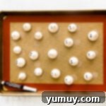 Ghost meringues lined up on a baking sheet, dotted with eyes.