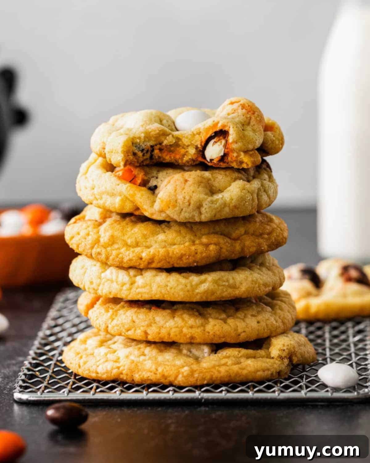 stack of halloween m&m cookies on a cooling rack, the top one is bitten.