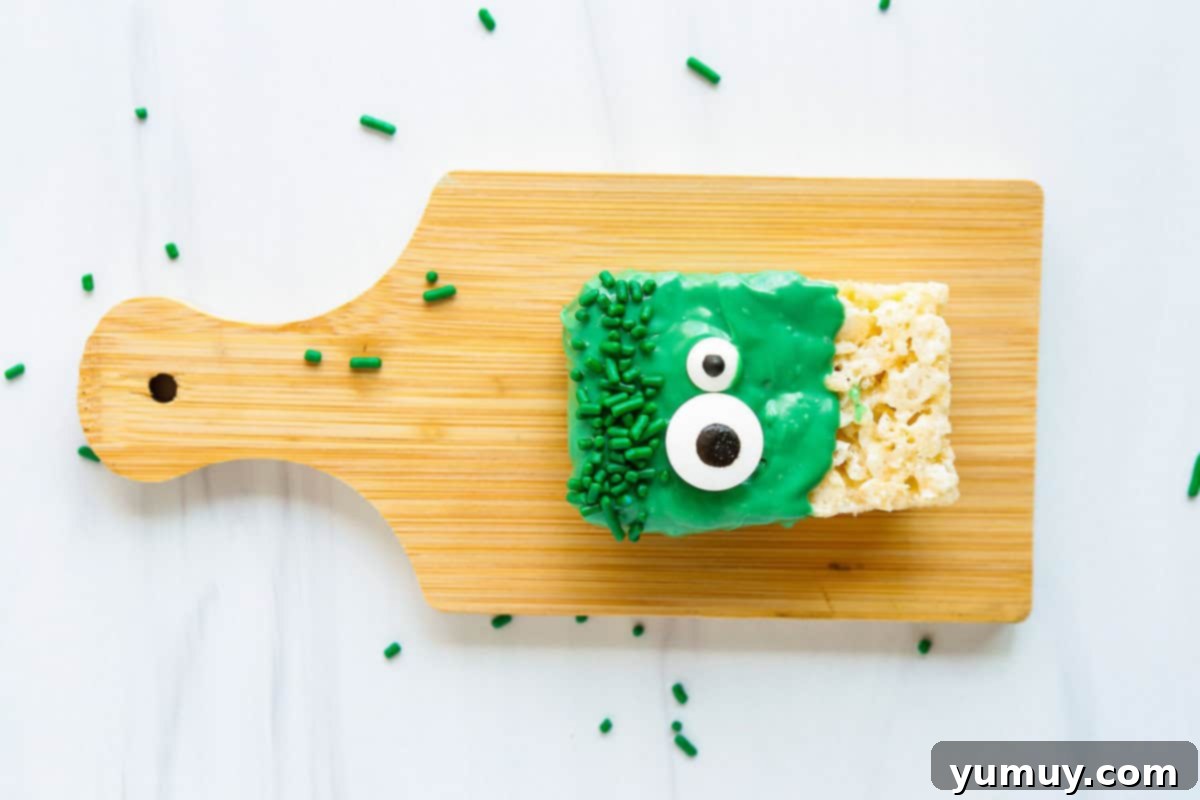 A completed Rice Krispie treat monster adorned with cheerful candy eyes, resting on a wooden tray with parchment paper, allowing the candy to set.