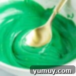 A bowl of vibrant green melted candy melts, perfectly smooth and ready for dipping Halloween monster Rice Krispie treats.