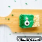 A freshly dipped Rice Krispie treat monster adorned with candy eyes and sprinkles, resting on parchment paper to set.