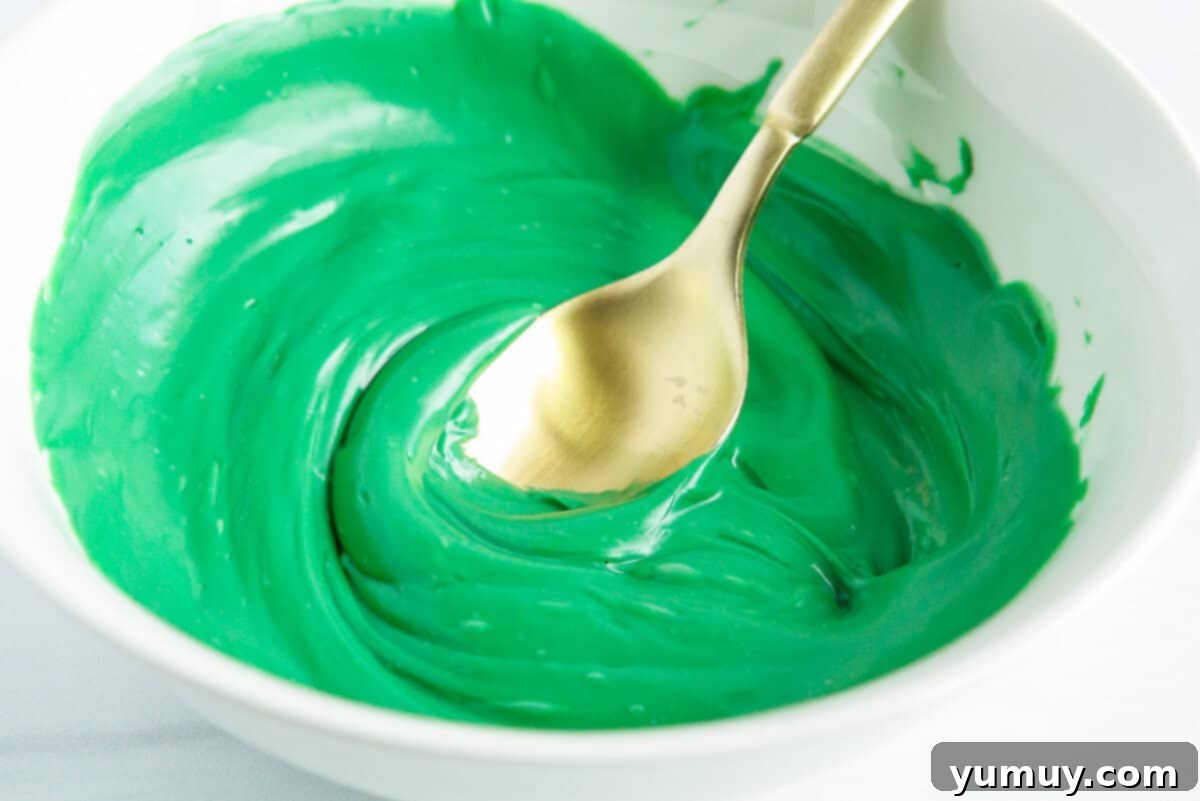 A bowl of vivid green melted chocolate, stirred to a smooth consistency, ready for dipping Rice Krispie treats.