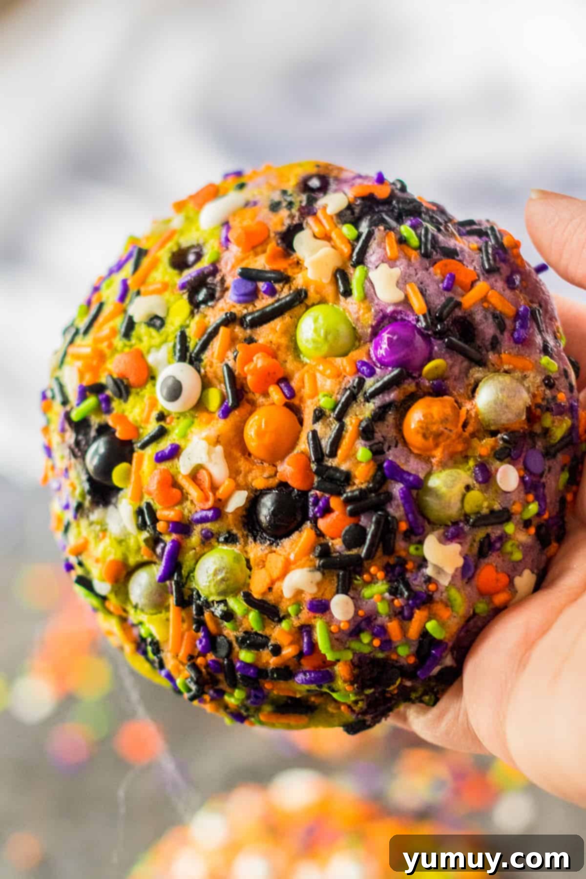 Holding up a vibrant Halloween sprinkle cookie, showcasing its marbled dough and colorful sprinkles.
