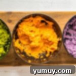 Three bowls of cookie dough, each dyed a different Halloween color: green, orange, and purple.