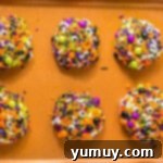 Cookie dough balls rolled in sprinkles on a baking sheet.