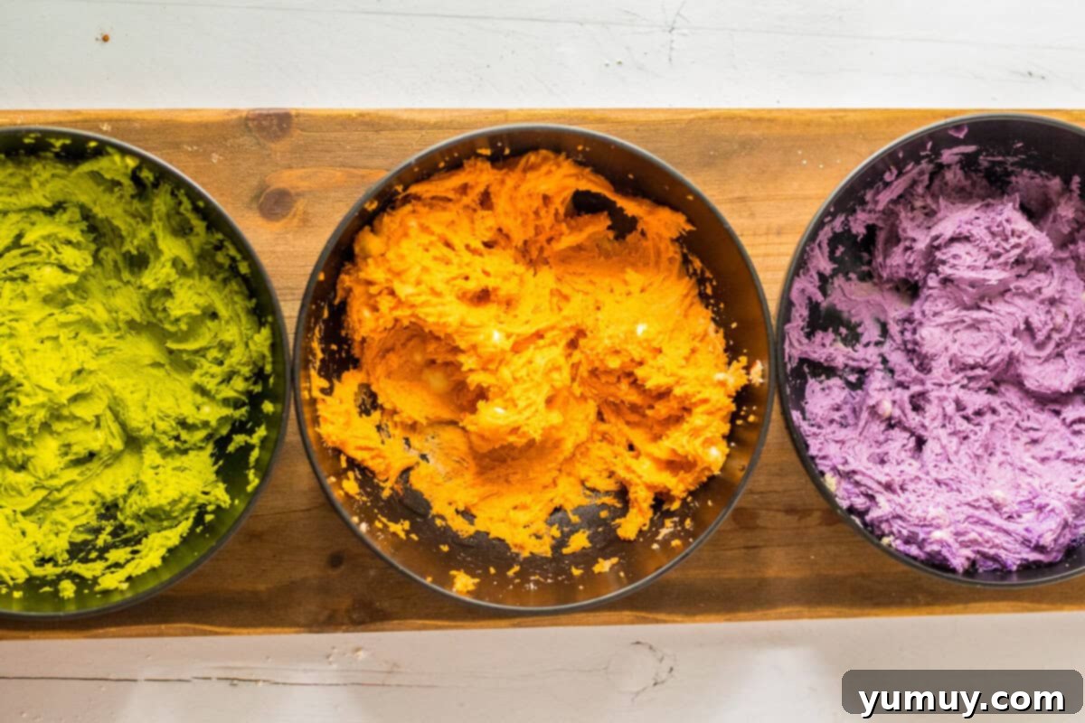 Cookie dough separated into bowls, each dyed a different Halloween color: green, orange, and purple.