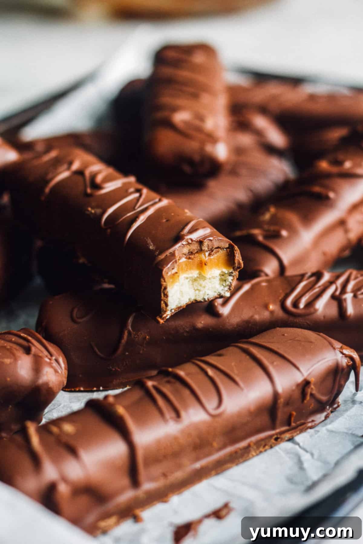 Homemade Twix bars showcasing layers of shortbread, caramel, and chocolate, arranged beautifully on parchment paper.