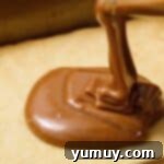 Pouring the perfectly melted caramel sauce over the cooled shortbread cookie base in the baking pan.