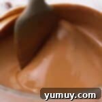 A bowl of glossy, melted chocolate being stirred to a smooth consistency, ready for dipping.