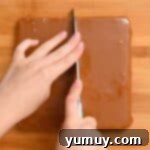 Precise slicing of the hardened caramel and cookie layers into uniform 1-inch bars on a cutting board.