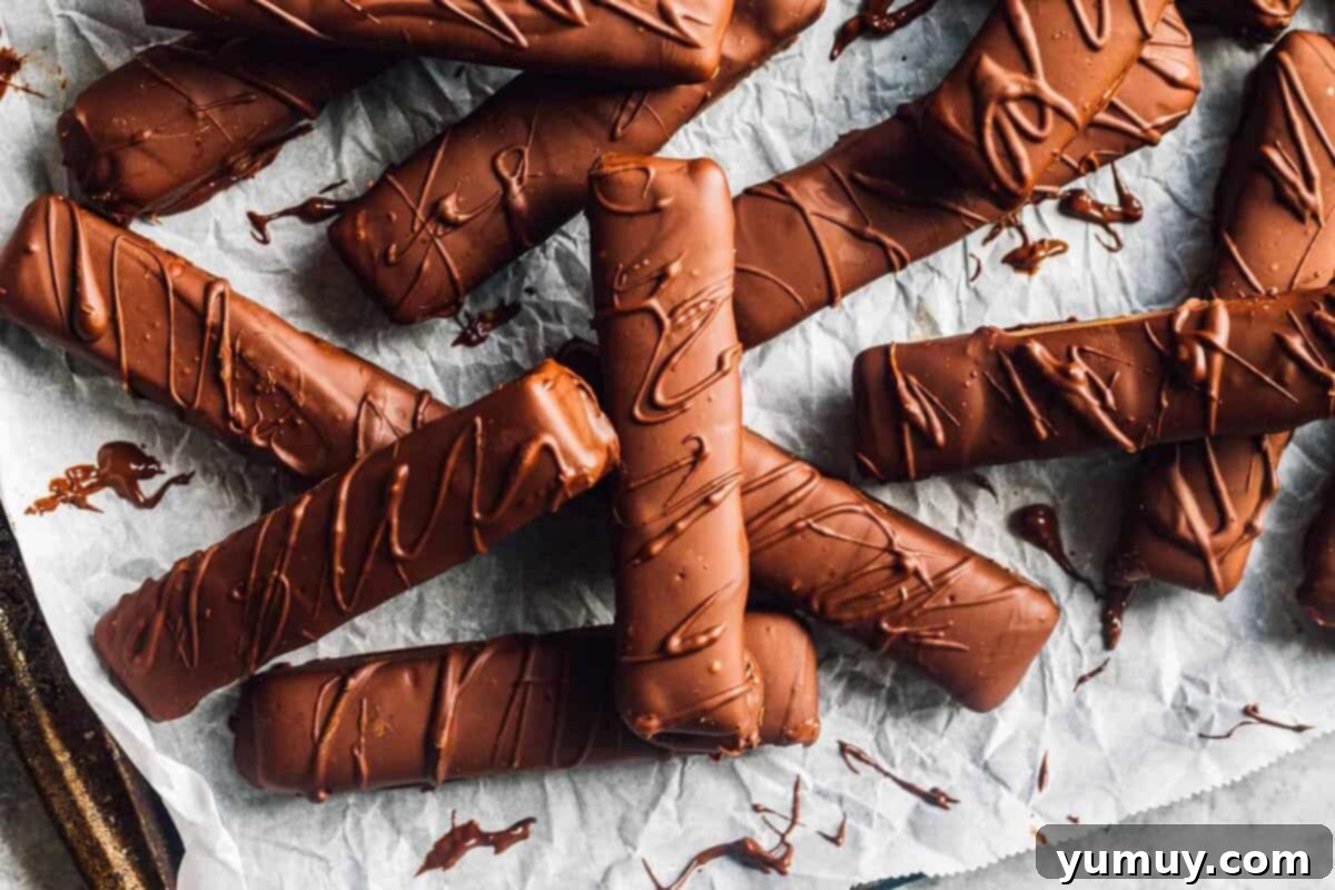 Close-up of freshly made homemade Twix candy bars, showing their distinct layers of cookie, caramel, and chocolate, arranged on parchment paper.