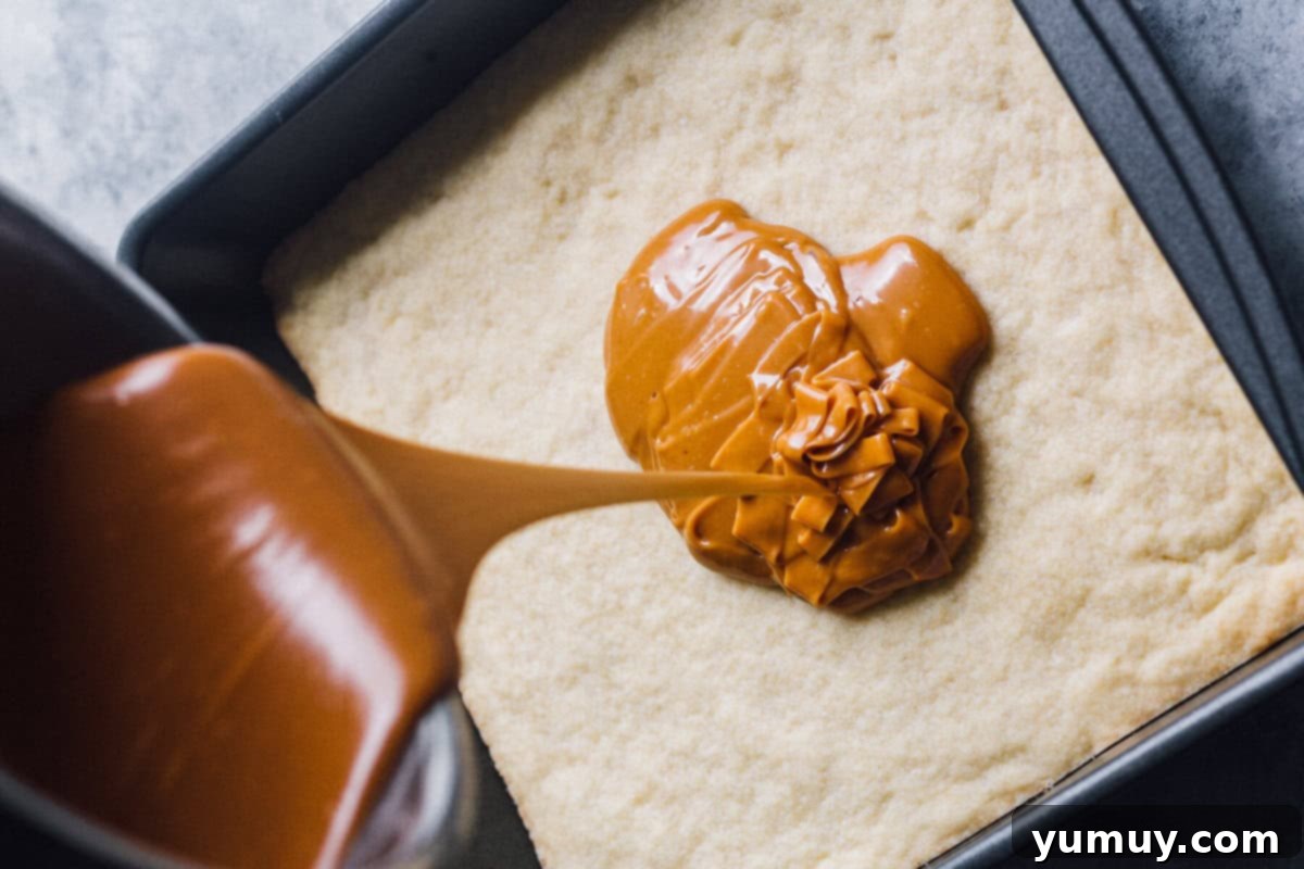Warm, golden caramel being smoothly poured over the perfectly baked shortbread base in a baking pan.