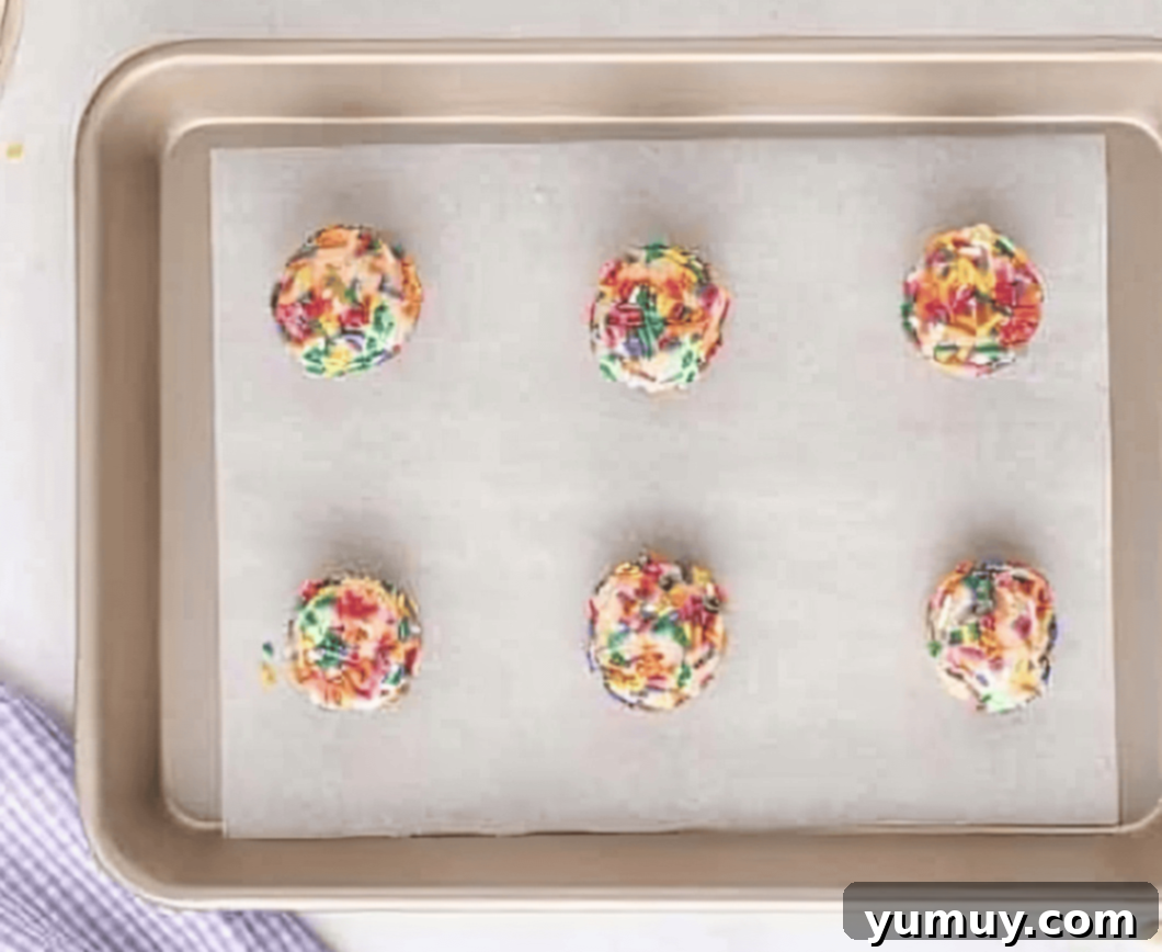 6 funfetti cookie dough balls on a baking sheet.