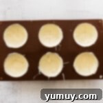 Coating silicone molds with melted white chocolate for hot cocoa bombs.