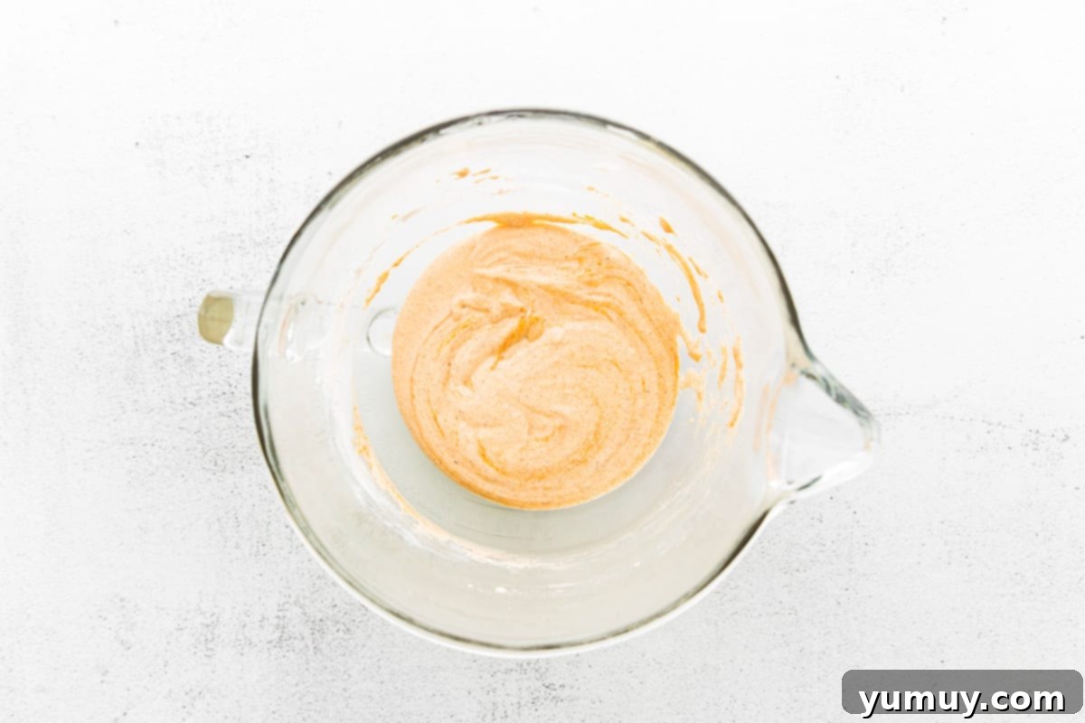 Prepared madeleine batter resting in a bowl inside a refrigerator, undergoing the essential chilling process for humps.