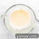 Eggs and sugar being vigorously beaten together in a stand mixer, forming a pale yellow, voluminous, and creamy mixture.