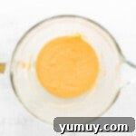 Melted and cooled unsalted butter being carefully folded into the madeleine batter using a rubber spatula.