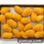 Freshly baked pumpkin madeleines with distinct humps cooling on a baking sheet before being transferred to a wire rack.