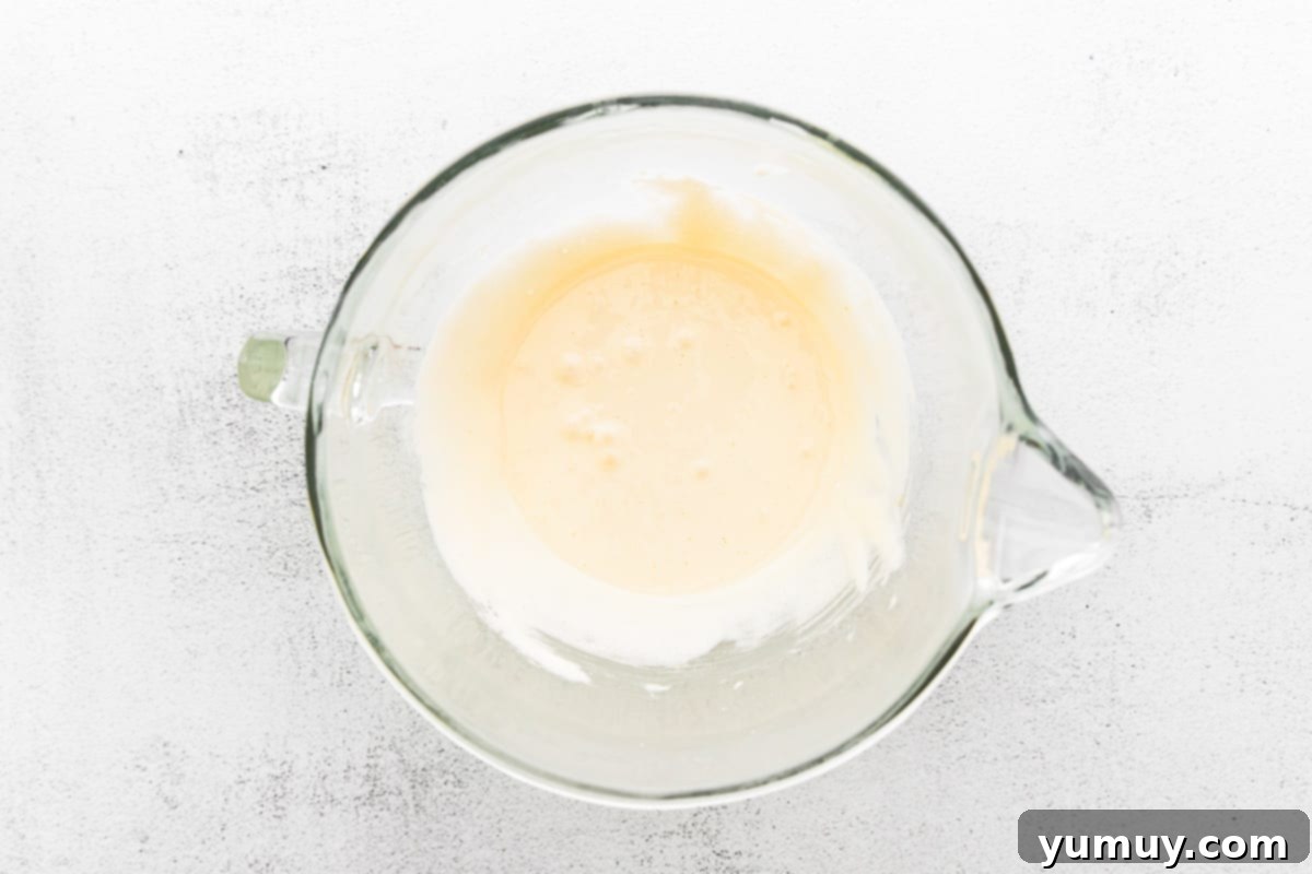 Close-up of eggs and granulated sugar being thoroughly beaten in a stand mixer, creating a light, airy, and pale yellow mixture.
