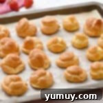 Freshly baked cream puffs on a lined baking sheet.