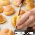 Cutting a cream puff in half hamburger bun style with a knife.