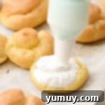 Piping sweetened whipped cream on the bottom half of a cream puff.