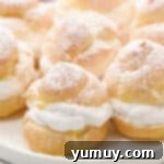 Dusting filled cream puffs with powdered sugar on a plate.