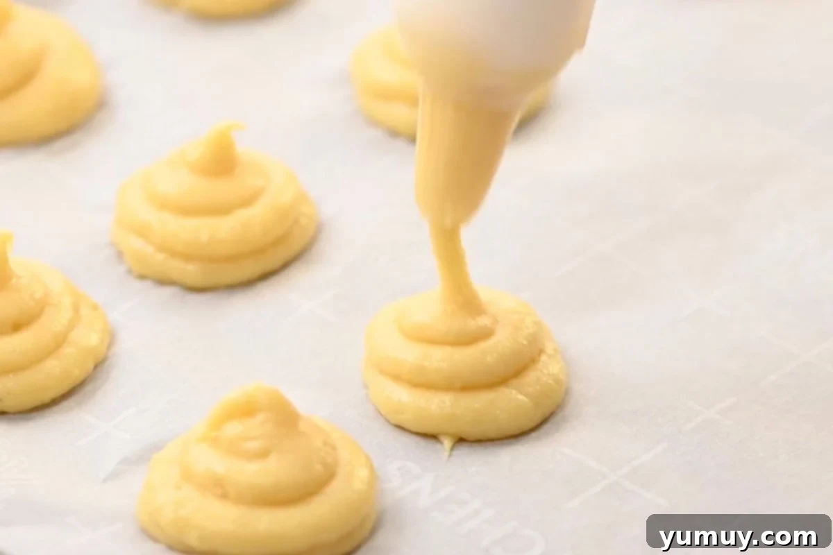 Piping cream puffs in a swirled pattern on a lined baking sheet.