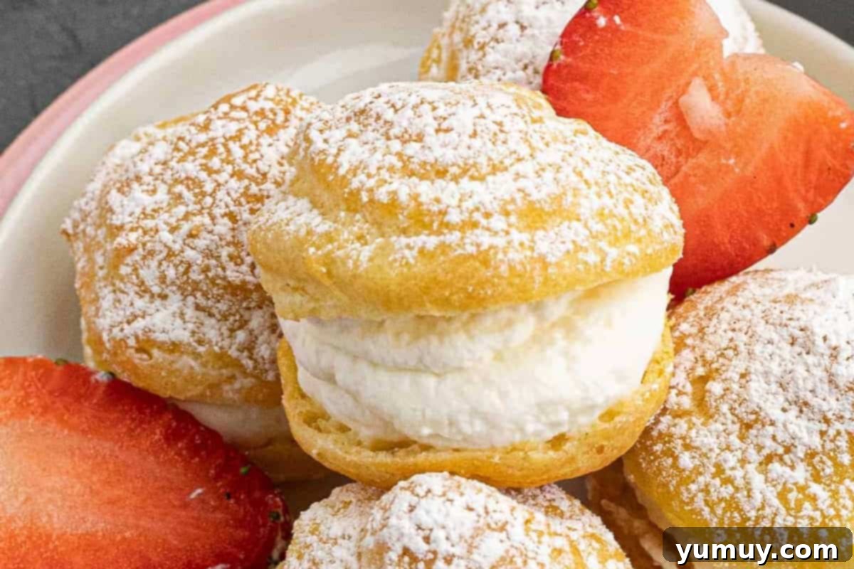 Closeup of a homemade cream puff on a plate with halved strawberries, showing the whipped cream filling.