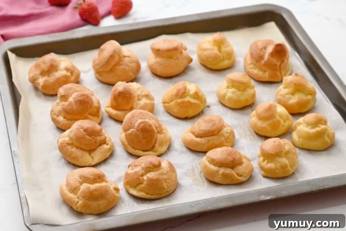 Freshly baked cream puffs cooling on a lined baking sheet.
