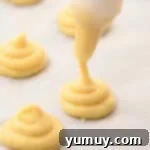 Piping cream puffs in a swirled pattern on a lined baking sheet.
