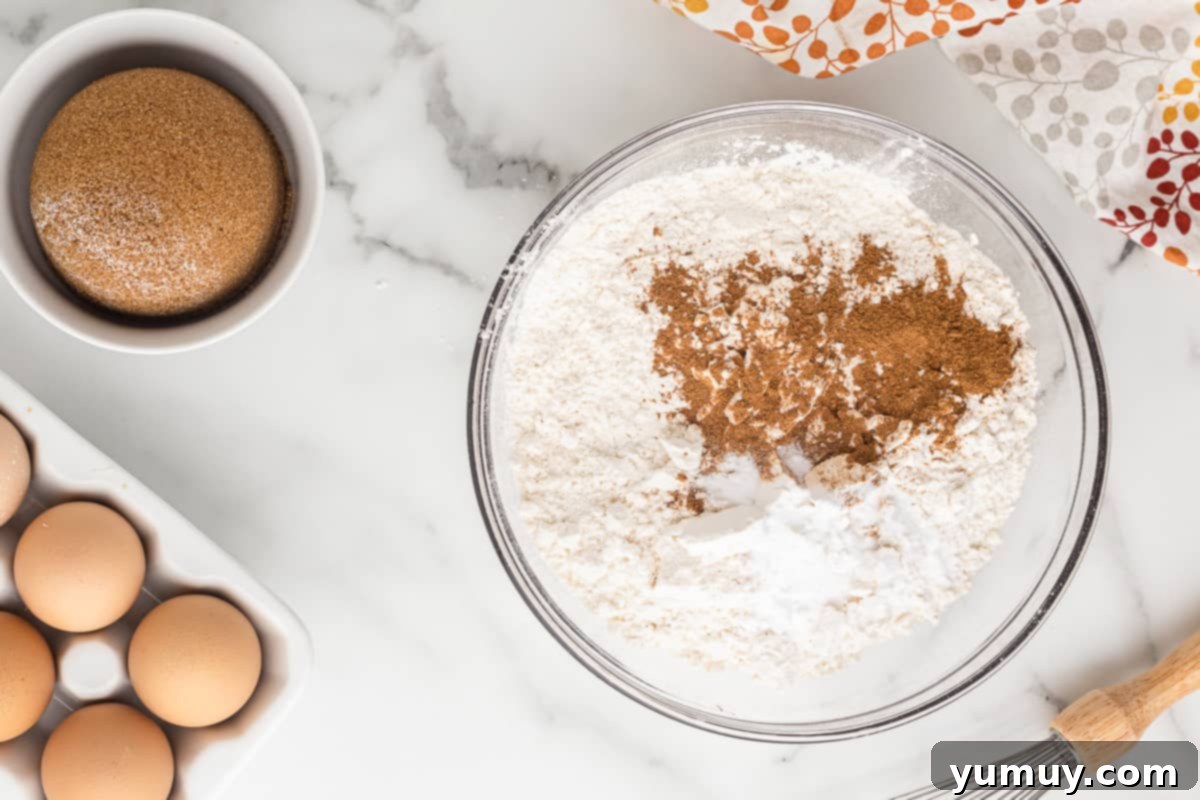 Dry ingredients like flour, pumpkin pie spice, and baking soda are thoroughly combined in a mixing bowl.