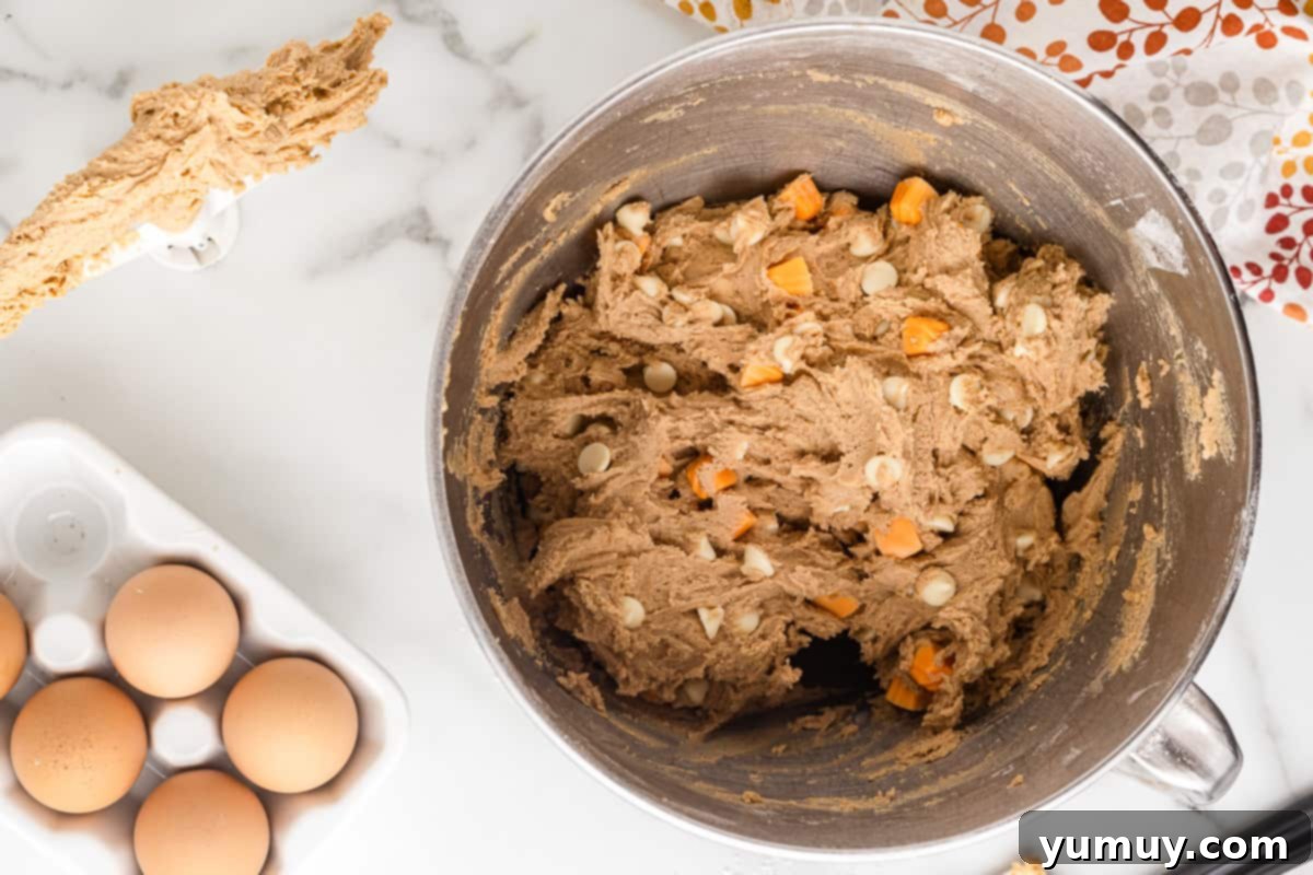The cookie dough, now with white chocolate chips and pumpkin spice chips folded in, showing a textured mixture.