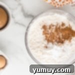 Dry ingredients like flour, pumpkin spice, and baking soda whisked together in a mixing bowl.