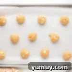 Balls of pumpkin spice cookie dough neatly arranged on a parchment-lined baking sheet before baking.